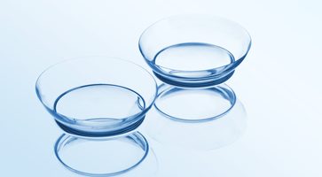 Two contact lenses Two contact lenses with reflections on a blue background. Focus on long-distance lens.